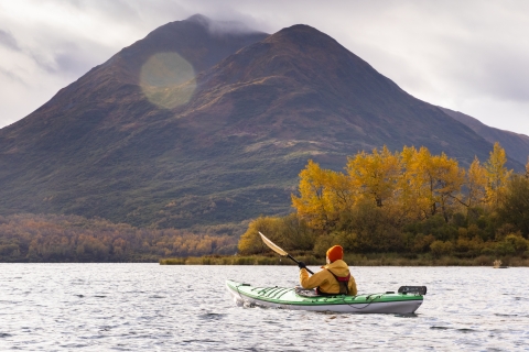 A woman kayaking on a lake with mountains and fall foliage in the background.