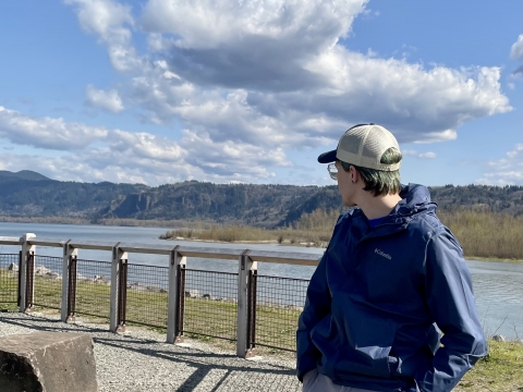 Person with baseball cap in a blue coat gazes out down the Columbia River looking east from the Refuge River Trail Overlook