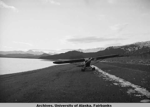 An Alaska Fish and Wildlife Service airplane sitting on a long beach with mountains in the background. 