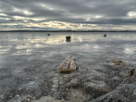 A close up of rocks sitting on top of a frozen lake with a dramatic, cloudy sky in the background.