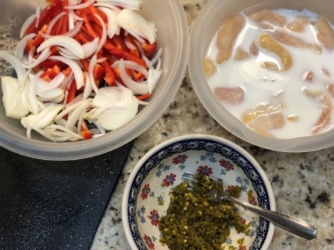 Three bowls with ingredients: peppers and onions on the left, green chilies in the middle, and pieces of fish soaked in milk on the right.