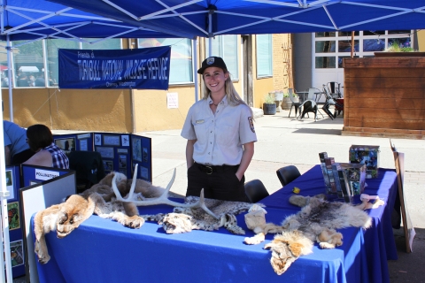 A female ranger wearing a brown and tan uniform staffs an outdoor information booth