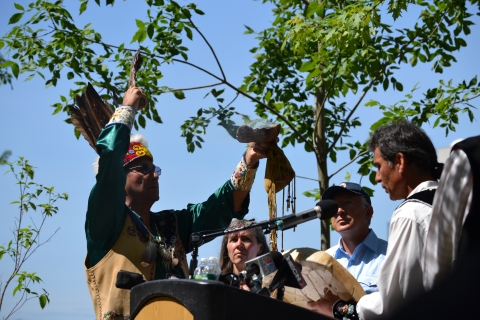 People gathered around a podium as one waves ceremonial objects and smoking sage. 