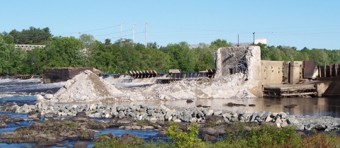 A photo of rocks and an crumbling concrete structure across a riverplain 