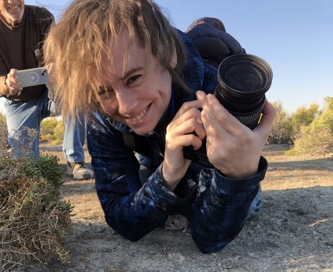 Cal Robinson lays on the ground with a camera in hand as a kangaroo rat hides under Cal's arms