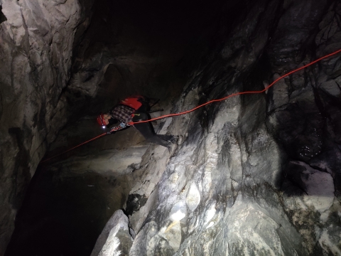 a person repels down a rope while inside a dark cave
