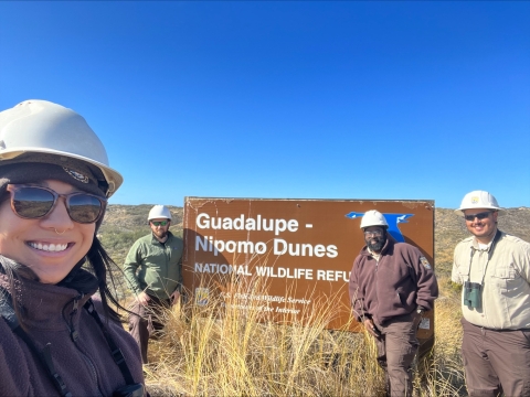 A group of people wearing hard hats pose with a sign that says Guadalupe Nipomo Dunes National Wildlife Refuge