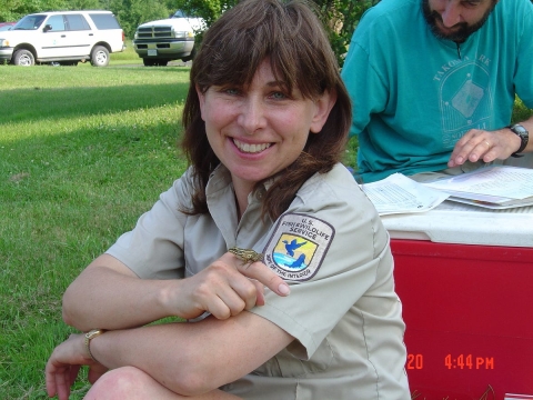 A person wearing a U.S. Fish and Wildlife Service uniform shirt, holds a small, spotted frog on her finger