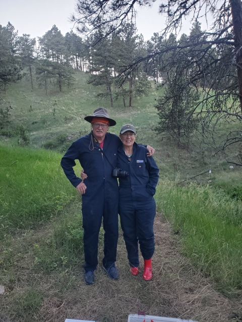 two people in blue jumpsuits pose together on a trail