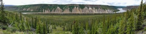 Panorama of a river curving around a bluff surrounded by boreal forest