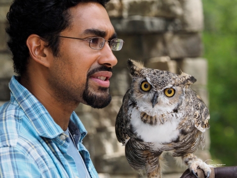 A man holds an owl which looks inquisitively at the viewer. 