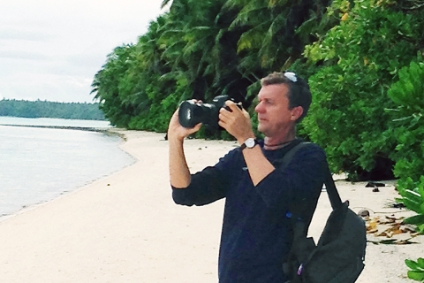 Person stands along shoreline with camera in hand.