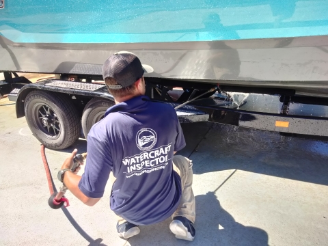 A watercraft inspection station staff member uses a pressure washer to clean the bottom of a watercraft