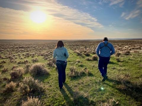 two people walking towards sunset through sagebrush landscape