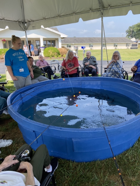 Elderly people fishing out of blue stock tub under a tent