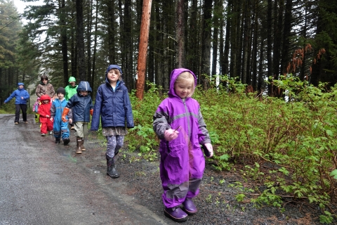 kids in multicolored rain gear walk down a gravel road