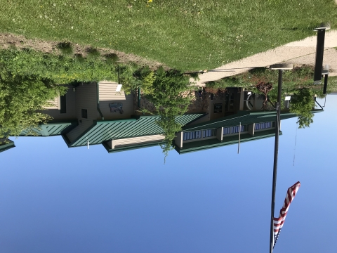 Brown building with green roof surrounded by native plants and American flag and flagpole
