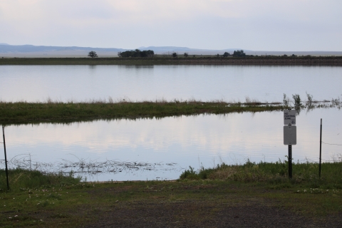 view of the lake 13 boat ramp with water, signs, and green grasses