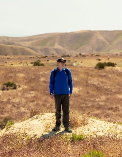 a man in a blue shirt stands on a dirt area on a plateau