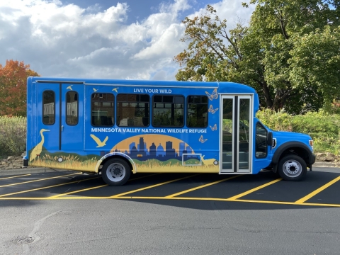 A bus painted blue with a city skyline and various birds and butterflies. The bus reads "Live your wild, Minnesota Valley National Wildlife Refuge"