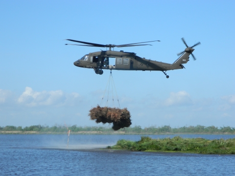 A helicopter drops a bundle of trees into a wetland