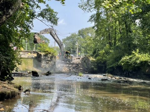 An excavator deconstructs a 12-foot-high dam