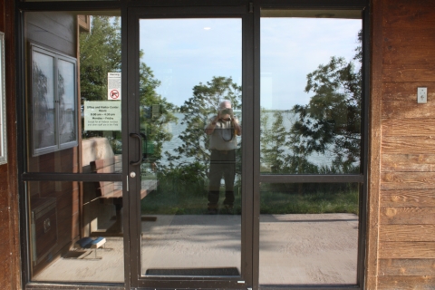 A person is reflected in the glass doors of a visitor center