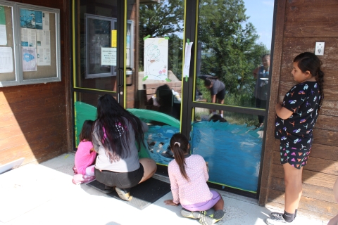 Three children work with an adult to illustrate a mural on the front doors of a visitor center