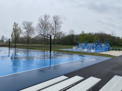 A new light and dark blue basketball court and outdoor exercise equipment within view of the river. 