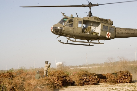 A man stands among bundles of trees as a helicopter hovers above
