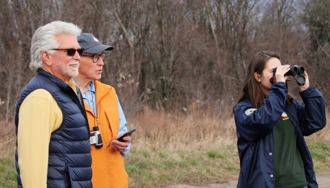 A woman looks through binoculars while two others look on.