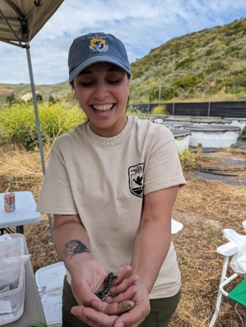 A woman in a baseball cap smiles as she holds a salamander in her hands