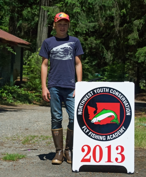 Jakob Bengelink posing next to a sign with the Northwest Youth Conservation and Fly Fishing Academy in 2013 when he was a camper.