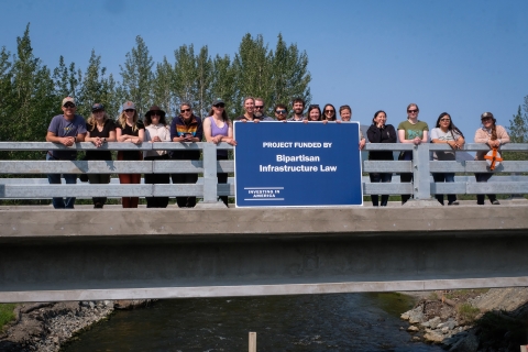 a group of people standing on a bridge over water holding a blue sign