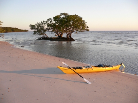A yellow kayak rests at an otherwise empty beach along the shore.