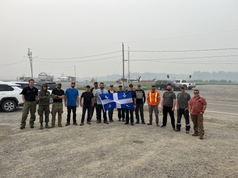 A group of individuals post for a photo at the airport among smoky skies.