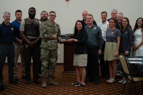 A man in fatigues accepts an award from a woman in a U.S. Fish and Wildlife Service shirt with a group of other people standing around them
