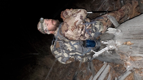 A man wearing hunting gear looks back into the camera while hunting at night
