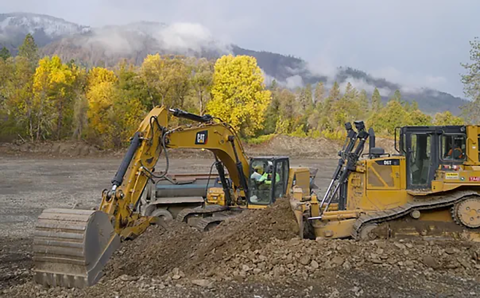 Heavy equipment with forest in the background moving large amounts of earth. 