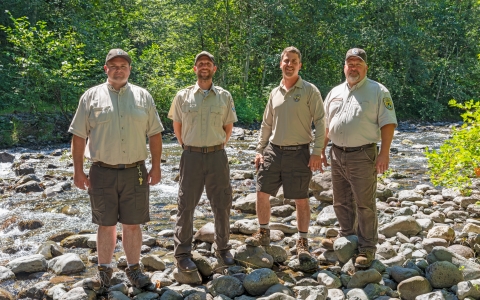Four Service staff members in uniform standing with the Big Quilcene River in the background.