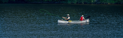 Two fly fishing academy campers fishing from a canoe on a lake. 