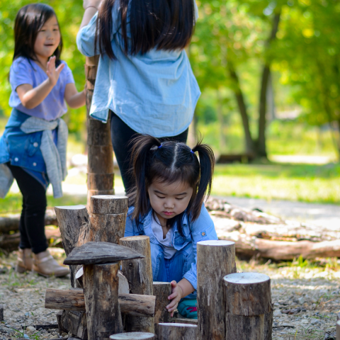 Three kids stack wood blocks while playing outside.