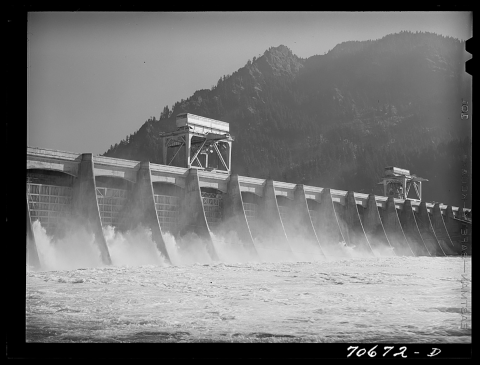 Noncolor image of a dam with a large mountain in the background. 
