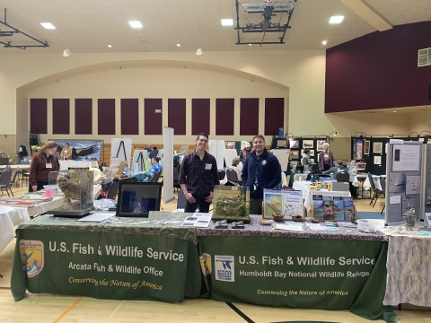 2 people standing behind an outreach table for the U.S. Fish & Wildlife Service inside an auditorium