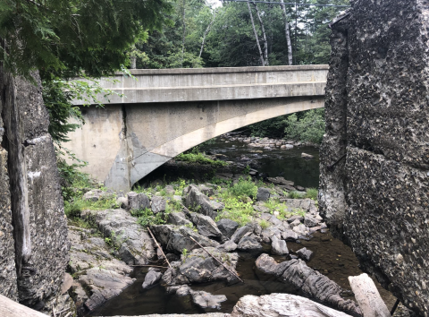 A concrete bridge over a low flow river with lots of large rocky debris.