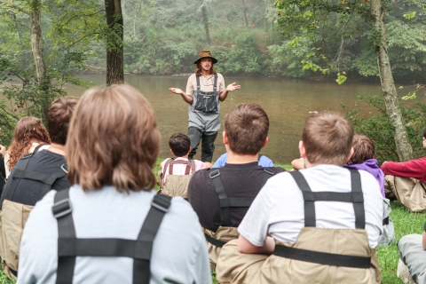 Person standing in front of a river addressing a group of young people