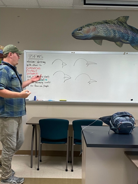 Man speaking in classroom with different bird beaks drawn on the marker board behind him