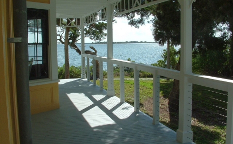 A house's partially shaded outside porch leads out toward the ocean.