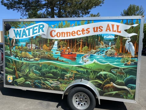 Trailer with wrap-around artwork depicting a river full of wildlife above and below the waterline, with people recreating and text that reads "Water Connects Us All"