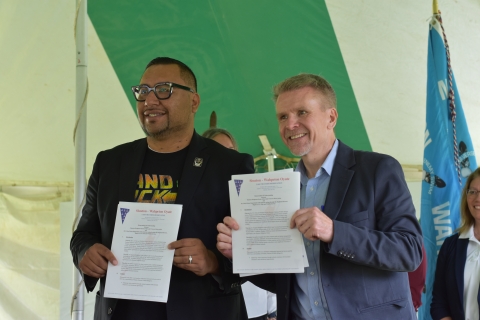 Two men hold up documents for the camera